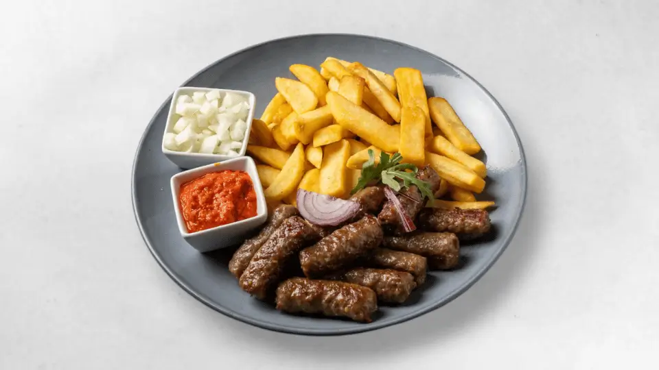 Zehn Cevapcici serviert mit Lepinja oder Pommes, Ajvar und Zwiebel, ideal für den großen Hunger