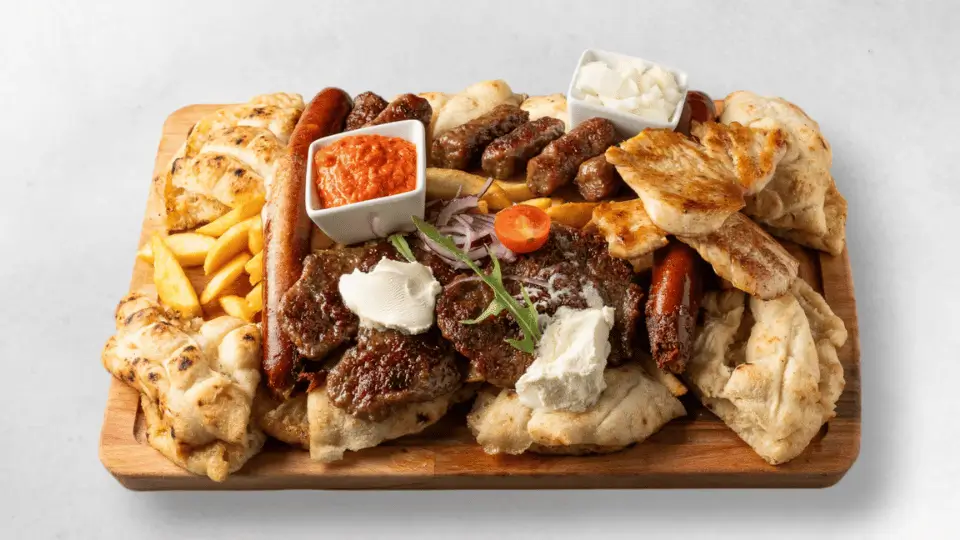 Grillplatte für zwei Personen mit 2 Würstchen, 2 Pljeskavica, 2 Hühnerfilet, 6 Cevapcici, 2 Chicken Wings, Pommes, Fladenbrot, Ajvar und Zwiebel