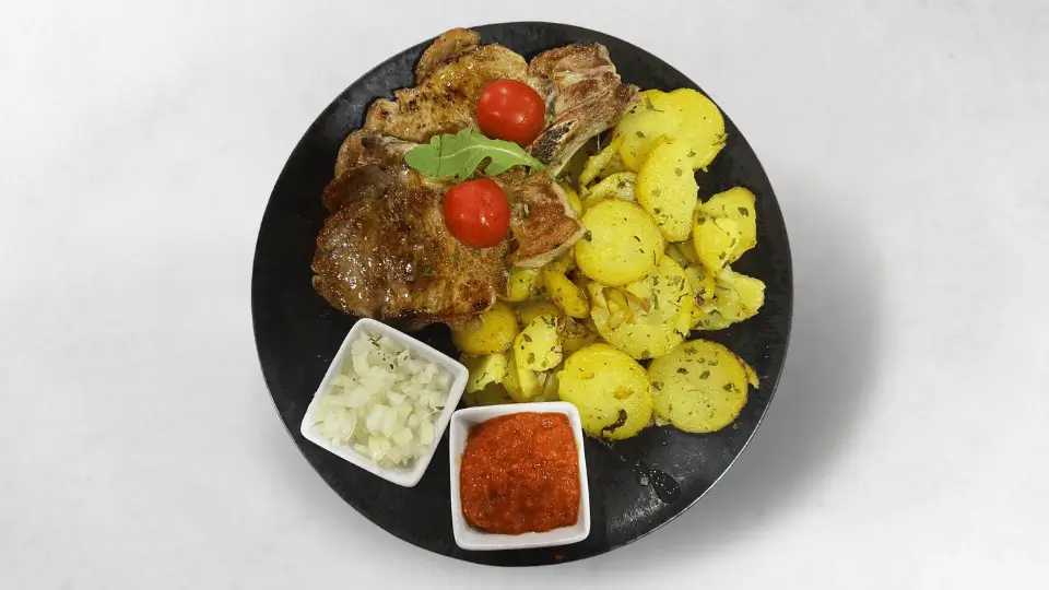 Zartes Kalbskotelett, perfekt gegrillt und serviert mit knusprigen Bratkartoffeln, würzigem Ajvar und frischen Zwiebeln für ein herzhaftes Geschmackserlebnis