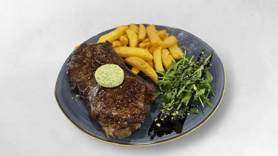 Rib-Eye Steak (280g) serviert mit Pommes und Kräuterbutter, ein Genuss für Fleischliebhaber.